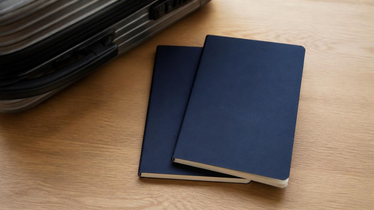 Deux carnets de voyage administratifs bleu marine posés sur une table à côté d'une valise cabine